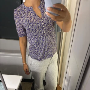 Blommig blus från H&M i lila och beige - Supersöt blus från H&M med lila och beige blommönster, korta ärmar och v-ringning med knappar framtill. Mjuk och tunn bomull som känns skön mot huden. Perfekt till jeans eller kjol. 💕