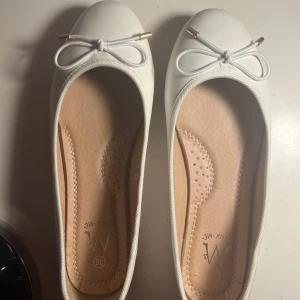 Vita ballerinaskor med rosett - Snygga vita ballerinaskor från Wink Me i storlek 38. Skorna har rund tå, platt sula och en söt rosett framtill med guldfärgade detaljer. Perfekt för dig som gillar stilrena och klassiska skor. Aldrig använt ute, bara testat.