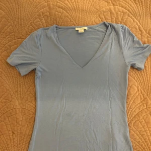 Ljusblå v-ringad topp från Amisu - Säljer en ljusblå topp från Amisu i storlek S. T-shirten har en snygg v-ringning och korta ärmar, perfekt för dig som gillar enkel och stilren design. Materialet är mjukt och stretchigt, vilket gör den skön att bära hela dagen.