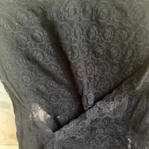 Svart blus linne  från H&M XS - Säljer en svart bluslinne från H&M i storlek XS. Klänningen är gjord i ett tunt spetsmaterial med blommigt mönster och har en omlott-detalj framtill. Perfekt för dig som gillar en feminin och elegant stil.