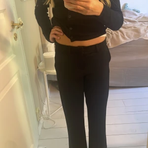 Svarta kostymbyxor med raka ben - Snygga svarta kostymbyxor med klassisk rak passform och lowwaist. Byxorna har bälteshällor och stängs med dragkedja och knapp. Byxorna är i storlek 1,52, och de är ifrån kaphal. Passar till både blus och t-shirt. Materialet är mjukt och har lite stretch för extra komfort.