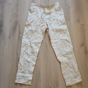 Beige linnebyxor från these glory days - Snygga beige linnebyxor med rak passform och snörning i midjan. Byxorna har knappstängning fram, elastisk midja bak och två bakfickor med knapp. Perfekta för chill dagar och sommarhäng. Luftigt material som ger en avslappnad vibe.