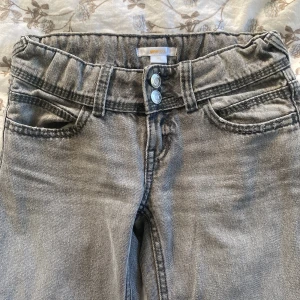 Grå wide jeans från Gina Tricot - Snygga grå jeans från Gina Tricot med två y2k knappar där bak. Modellen är wide med raka ben. Perfekt för dig som gillar trendig stil. 