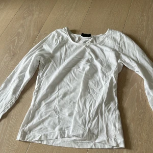Vit långärmad tröja från LMTD - En enkel och fräsch vit långärmad tröja från LMTD i storlek S, passar dig som gillar clean och basic stil. Tröjan har rund hals och är gjord i mjuk bomull, perfekt för lager-på-lager eller bara som den är. Snygg att matcha med jeans eller kjol.