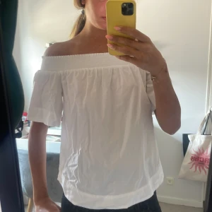 Vit offshoulder blus med kort ärm - Säljer en fräsch vit blus med offshoulder-design och korta ärmar. Toppen har en bred resår upptill som håller den på plats och ger en snygg siluett. Perfekt för varma dagar och enkel att matcha med jeans eller kjol.