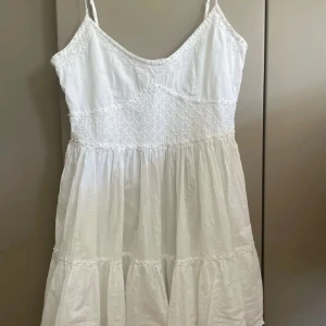 Vit  linne med broderi - Säljer en vit linne  med tunna axelband och v-ringad hals. Överdelen har fint broderat mönster och pärldetaljer, medan kjolen är volangig och luftig. Perfekt för varma dagar och har en romantisk vibe. 