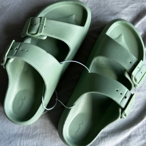 Gröna sandaler från HappyFlops - Snygga ljusgröna sandaler från HappyFlops med två breda remmar och justerbara spännen.           Storlek 38, upplever dom något mindre i storlek. Helt nya, endast testade! 