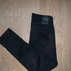 Replay Anbass svarta jeans - Svarta Replay Anbass jeans med slim passform och klassisk femficksdesign. Modellen är Hyperflex X.L.I.T.E. Re-used, vilket ger extra stretch och komfort. Snygga detaljer med svarta sömmar och diskret Replay-logga på bakfickan. Perfekta för dig som gillar stilrena och moderna jeans.