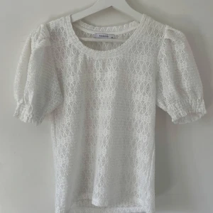 Vit spetsblus från Reserved XS - Supersöt vit blus från Reserved i storlek XS. Blusen har puffiga korta ärmar med resår och är helt täckt av ett detaljerat spetsmönster. Rund halsringning och lätt transparent look ger en fräsch vibe. Perfekt för dig som gillar romantisk stil och snygga detaljer.