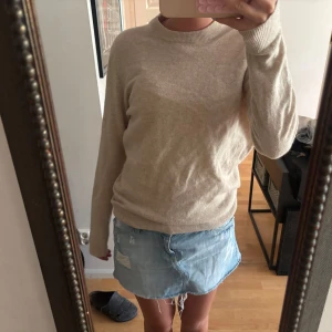 Beige stickad tröja med rund hals - Säljer en enkel och snygg beige stickad tröja med rundad hals och ribbade muddar vid ärmslut och nederkant. Tröjan har en normal passform och är långärmad, perfekt att slänga på sig när det är lite kyligt ute.