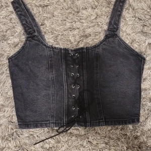 Svart jeanskorsett från Wild Fable XS - Cool svart korsett-topp från Wild Fable i jeansmaterial. Croppad modell med breda axelband, snörning framtill och dragkedja bak.