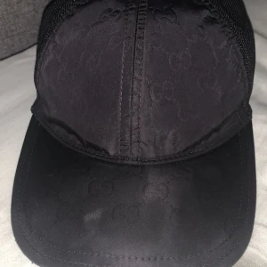 Gucci keps Nylon - Snygg svart keps från Gucci med diskret GG-mönster på framsidan och mesh på sidorna för extra ventilation. Justerbar baktill och stilren design som lyfter din outfit. Perfekt för dig som gillar exklusiva accessoarer med streetkänsla.