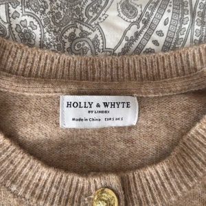 Randig beige kofta från Holly & Whyte - Superfin beige och svart randig stickad kofta från Holly & Whyte med guldknappar framtill. Typ aldrig använd och köpt på Lindex för några år sen. Storlek S!💖