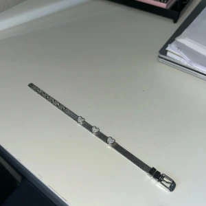 Silverfärgat armband med hjärtan - Snyggt armband i silverfärg med fem glittriga hjärtan som dekoration. Armbandet har ett meshband och ett klassiskt spänne som gör det enkelt att justera storleken. Perfekt för dig som gillar detaljer med lite extra bling och romantisk vibe.
