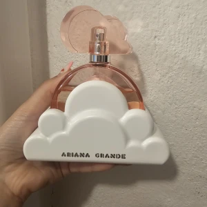 Ariana Grande Cloud parfym - Superfin parfym från Ariana Grande i modellen Cloud. Flaskan är rund och genomskinlig med en svagt rosa ton och har ett lock i form av ett moln. Parfymen kommer med en vit molnformad hållare i plast. Perfekt för dig som gillar söta och fräscha dofter.