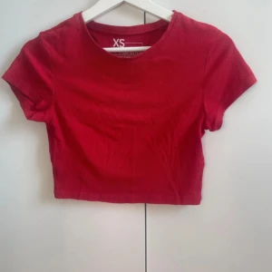 Röd croppad topp från FSBN Sister - Snygg röd croppad topp från FSBN Sister (newyourker) i ribbad bomull. Modellen har rund hals och korta ärmar, perfekt för dig som gillar en enkel men trendig look. Passformen är kort till magen och materialet är mjukt och stretchigt. Supersnygg att matcha med höga jeans eller kjol.