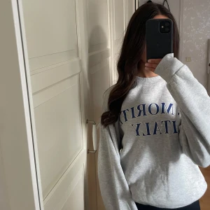 Grå sweatshirt St. Moritz Italy - Säljer en grå sweatshirt med blå text 'ST. MORITZ ITALY' på bröstet. Tröjan har rund hals, ribbade muddar och är långärmad. Perfekt för chill dagar och enkel att matcha med jeans eller leggings. Materialet är mjukt och känns skönt mot huden.