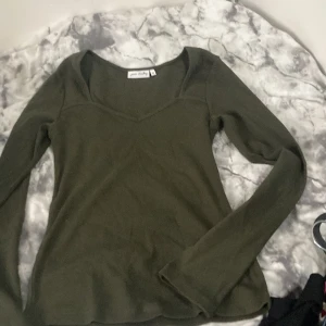 Olivgrön långärmad tröja Pure Friday - Snygg olivgrön långärmad tröja från Pure Friday i storlek M. Tröjan har en v-ringad hals och är tillverkad i mjuk, ribbad bomull som sitter skönt mot kroppen. Perfekt att matcha med jeans eller kjol för en chill look. Passar bäst som S-M