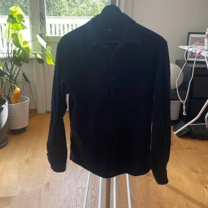 Mörkblå manchester overshirt Uniqlo  - Snygg mörkblå overshirt från Uniqlo i mjuk manchester. Klassisk krage, bröstficka och knappar framtill. Perfekt att slänga på över en t-shirt för en chill look. Passar dig som gillar stilrena och enkla plagg med lite edge. Storlek XS men sitter mer som en S skriv vid funderingar 
