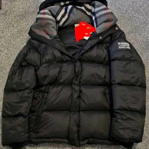 Svart dunjacka från Burberry - Snygg svart dunjacka från Burberry med klassiskt rutigt foder i huvan. Jackan har en puffig siluett, dragkedja och knappar framtill samt Burberry-logga på ärmen. Perfekt för kalla dagar när du vill hålla stilen.