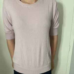 Ljusrosa stickad tröja med kort ärm - Snygg ljusrosa stickad tröja med rund hals och korta ärmar. Tröjan har en mjuk och tunn stickning som gör den skön att bära. Passar perfekt till jeans eller kjol och har en enkel, stilren look som är lätt att matcha.