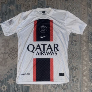 Helt ny vit psg t shirt  storlek S/M - Snygg PSG fotbollströja i vitt med mörkblå och röda vertikala ränder på framsidan. Tröjan har korta ärmar, rund hals och tryck med Qatar Airways samt Paris Saint-Germain-logga. Tillverkad i lätt och ventilerande material, perfekt för träning eller match.