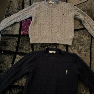 Grå och marinblå stickad tröja polo. Storlek XS på båda.   - Två snygga kabelstickade tröjor från Polo Ralph Lauren, en i grått och en i marinblått. Båda har rund hals, lång ärm och den klassiska broderade loggan på bröstet. Perfekt för dig som gillar stilrena och tidlösa plagg med skön passform. Båda tröjorna är till storlek XS. Fastän det står på tröjorna S och M så stämmer det inte alls överens, tröjorna är små och passar för XS.😊