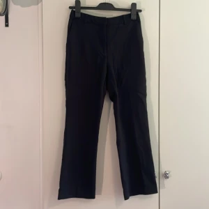 Svarta kostymbyxor  - Snygga svarta kostymbyxor med rak passform. Byxorna har bälteshällor och är tillverkade i ett slätt material som ger en stilren look. Perfekta för dig som gillar en clean och enkel stil.