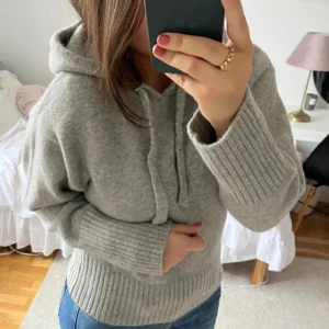 Grå stickad hoodie med snörning - Mysig grå stickad hoodie med huva och snörning framtill. Tröjan har breda ribbade muddar vid ärmslut och nederkant. Tröjan har inga defekter eller liknande💕(Lånad bild)