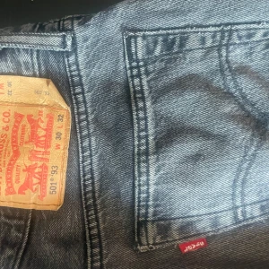 501 Levis jeans  - Säljer ett par Levi's 501 jeans i mörk grå tvätt med klassisk straight fit och knappgylf. Jeansen har fem fickor, röd Levi's-tag på bakfickan och snygga kontrastsömmar. Finns ett jättelitet hål i nära juvelen men det är lätt att lappa ihop.