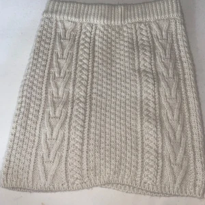 Stickad beige kortkjol från Lindex - Supermysig stickad kjol från Lindex i beige färg. Kjolen är kort och har snygga flätstickade detaljer och ribbad midja. Perfekt att matcha med en oversized tröja och boots för en chill look.