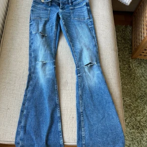 Bootcut jeans med slitningar Gina Tricot - Blå bootcut jeans från Gina Tricot i storlek XS. Modellen har slitna detaljer vid knäna och framsidan, klassiska fickor både fram och bak samt dragkedja och knapp. Jeansen har en snygg utsvängd passform och är gjorda i jeansmaterial.