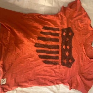 Ljus röd t-shirt från American Vintage - Säljer en ljus röd t-shirt från American Vintage med ett unikt tryck på framsidan. T-shirten är kortärmad och gjord av mjuk bomull.