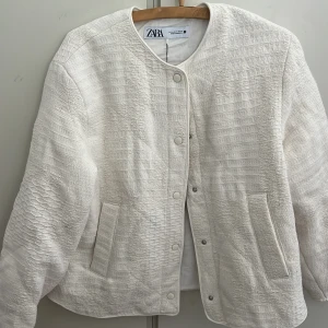 Vit quiltad jacka från Zara - Snygg vit quiltad jacka från Zara med rund hals och knappar framtill. Jackan har en stilren design med två fickor och en texturerad yta som ger en unik look. Perfekt för att lyfta din outfit!