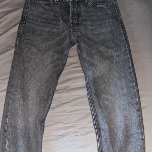 Grå jeans från Jack & Jones - Säljer ett par grå jeans från Jack & Jones i modellen Loose/Chris. De har en loose passform och är tillverkade i denim. Klassisk femficksdesign med knappgylf och bälteshällor. Knappt använda
