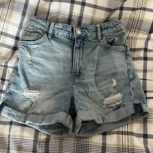 Blå jeansshorts från H&M - Säljer ett par coola blå jeansshorts från H&M. De har en avslappnad passform och är högmidjade med slitna detaljer för en trendig look. Perfekta för sommardagar! 🌞