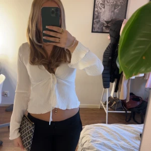 Vit ribbad knytblus - Säljer en snygg vit ribbad blus med knytning framtill. Blusen har långa ärmar och en croppad passform som ger en trendig look. Perfekt för att styla med både jeans och kjol.