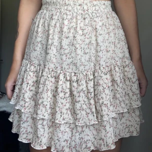 Blommig volangkjol från NAKD - Charmig blommig kjol från NAKD  med volanger och elastisk midja. Perfekt för en somrig look med sitt lätta och luftiga material. Den har ett sött blommönster i ljusa färger som ger en romantisk känsla. Är villig till att sänka pris!!!!