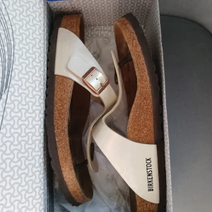Btirkenstock strl 41 - Säljer ett par vita Birkenstock Gizeh sandaler i modellen 'Graceful Pearl White'. De har en bekväm korksula och justerbart spänne i metall. Perfekta för sommarens äventyr! Fint skick 