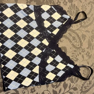 Rutig linne med spetsdetaljer - Snyggt linne med rutigt mönster i svart, blått och vit. Toppen har spetsdetaljer vid halsringningen och smala axelband. Perfekt för en trendig look!