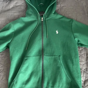 Grön hoodie från Ralph Lauren - Säljer en snygg grön hoodie från Ralph Lauren med dragkedja och klassisk logga på bröstet. Tröjan har en justerbar huva och praktiska fickor framtill. Perfekt för en avslappnad stil! 💚