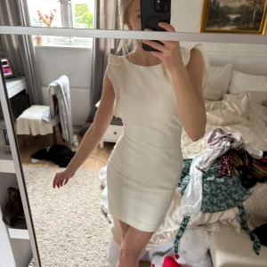 Vit kort klänning med volangdetaljer - Säljer en stilren vit kort klänning med volangdetaljer vid ärmarna och en öppen rygg. Klänningen har en tight passform och en dragkedja i ryggen för enkel påklädning. Perfekt för sommarens festligheter som student och midsommar. Klänningen framhäver kroppen och skadar kurvor man inte ens visste att man hade😍 Hade behållt den om den inte börjar bli för liten för mig😔Storleken står på sista bilden men tror det är XS-S!