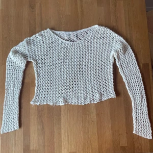 Vit stickad tröja - Säljer en vit stickad tröja med ett öppet nätmönster. Tröjan har en croppad design och långa ärmar. 