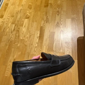 Svarta loafers från Ralph Lauren - Snygga svarta loafers i skinn från Ralph Lauren. Klassisk design med rund tå och diskret logotyp på sidan. OBS: Hade extra sulor inuti skorna som på något sätt klistrade fast i originalsulan, därav märkena på innersulan då jag fått skrapa bort rester. Annars i nyskick o använda endast 2 gånger. Nypris 2600 och Köpta på Volt för cirka 3 mån sen. Storlek 42 (passar om du har 43 i vanliga skor).