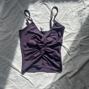 Lila ribbad linnetopp - Säljer en snygg lila ribbad linnetopp med smala axelband och en twistdetalj framtill. Perfekt för fest