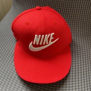 Röd keps från Nike - Snygg röd keps från Nike med broderad vit logga framtill. Perfekt för en sportig look eller som en stilren accessoar. Justerbar passform för optimal komfort.