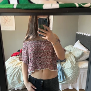 Blommig offshoulder topp - Säljer en söt blommig offshoulder topp från H&M Divided. Toppen är croppad och har en elastisk passform med korta ärmar. Perfekt för varma dagar!