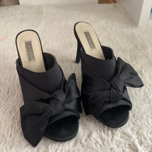 Svarta klackskor med rosett ✨ - Eleganta svarta klackskor från NLY Shoes med en stilren rosett på ovansidan. Skorna har en öppen tå och en smal klack som ger en sofistikerad look. Perfekta för att lyfta din outfit till nästa nivå.