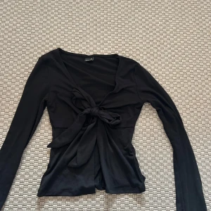 Svart långärmad topp med knyt - Snygg svart långärmad topp från gina med knyt framtill. Perfekt för en stilren look. Passar bra till både jeans och kjol.