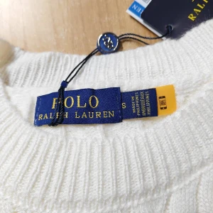 Vit stickad tröja från Polo Ralph Lauren - Säljer en stilren vit stickad tröja från Polo Ralph Lauren med det klassiska broderade logotypen på bröstet. Tröjan har en kabelstickad design och långa ärmar, Passar både till jeans och chinos!